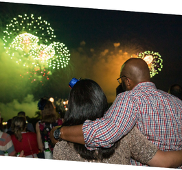 Two individuals with arms around each other watching green fireworks 